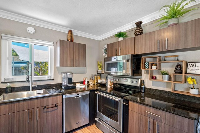 kitchen featuring dark stone counters, light wood-style flooring, a sink, ornamental molding, and appliances with stainless steel finishes