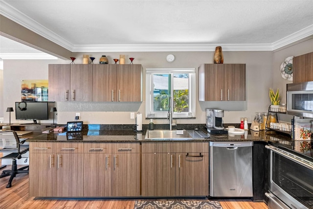 kitchen featuring dark stone counters, a sink, stainless steel appliances, light wood-style floors, and crown molding