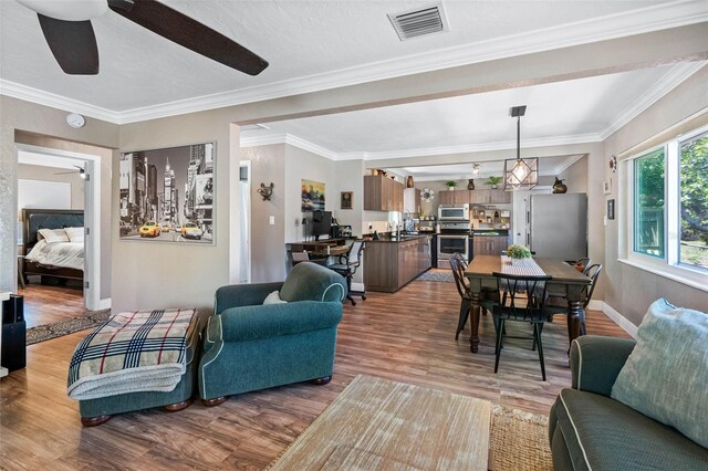 living area with ceiling fan, visible vents, wood finished floors, and crown molding