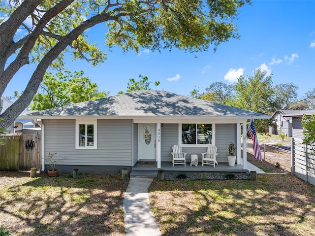 view of front of property with covered porch, a shingled roof, a front yard, and fence