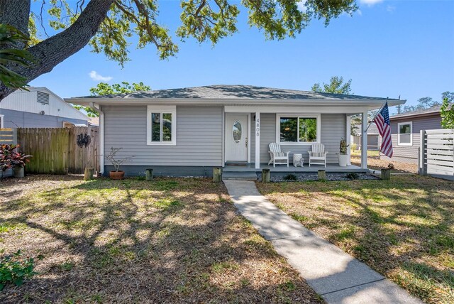 bungalow-style home featuring covered porch, a front lawn, and fence