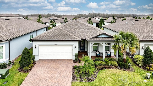 single story home featuring a residential view, roof with shingles, covered porch, decorative driveway, and an attached garage