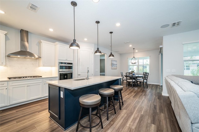 kitchen with visible vents, a sink, decorative backsplash, appliances with stainless steel finishes, and wall chimney range hood