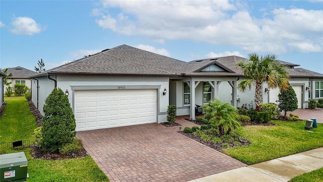 ranch-style home featuring decorative driveway, a front lawn, an attached garage, and stucco siding