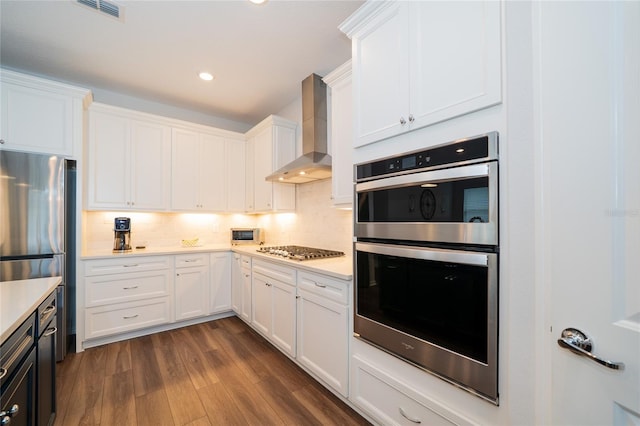 kitchen with dark wood-type flooring, backsplash, white cabinetry, stainless steel appliances, and wall chimney exhaust hood