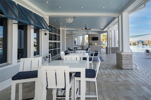 view of patio with outdoor dining area, an outdoor stone fireplace, and ceiling fan