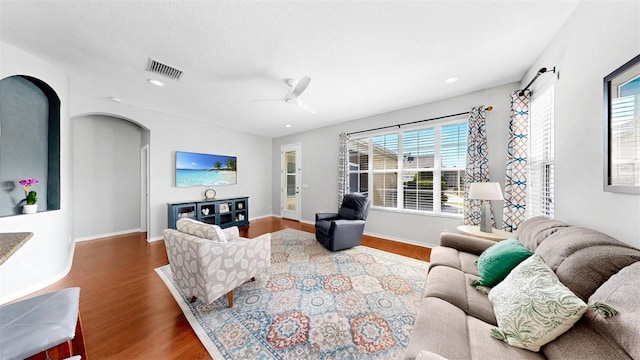 living area with arched walkways, wood finished floors, visible vents, baseboards, and a ceiling fan