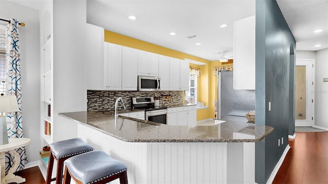 kitchen with stainless steel appliances, a peninsula, dark wood-style floors, decorative backsplash, and dark stone counters