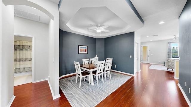 dining space featuring a raised ceiling, wood finished floors, a ceiling fan, and baseboards