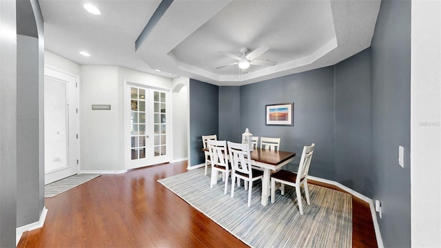 dining space with a ceiling fan, a tray ceiling, baseboards, and wood finished floors