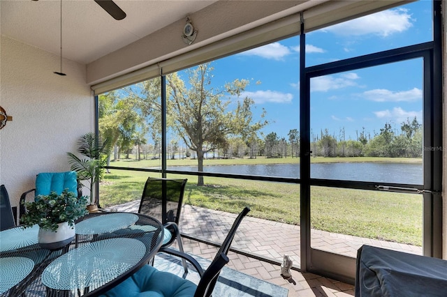 sunroom with ceiling fan and a water view