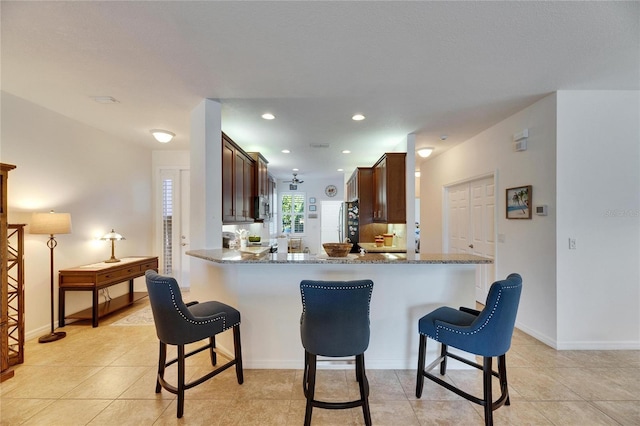 kitchen with stainless steel microwave, a breakfast bar area, a peninsula, and stone countertops