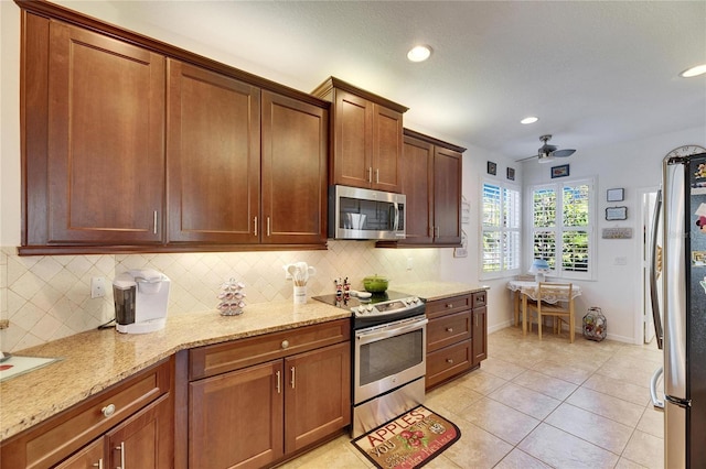 kitchen with backsplash, light stone countertops, light tile patterned floors, stainless steel appliances, and a ceiling fan