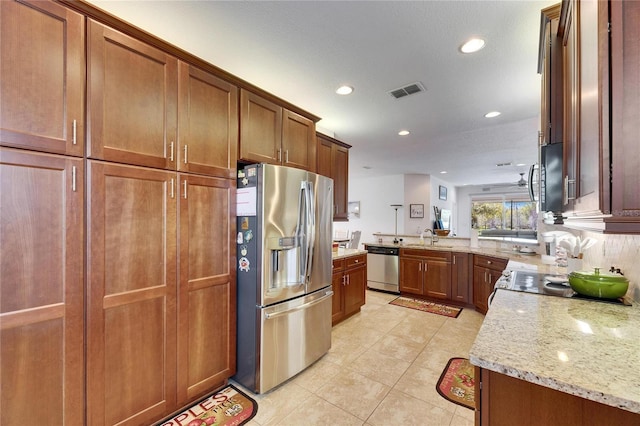 kitchen with visible vents, light stone countertops, appliances with stainless steel finishes, brown cabinetry, and a sink