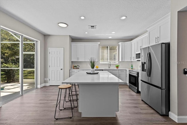 kitchen featuring visible vents, a kitchen bar, a sink, white cabinetry, and appliances with stainless steel finishes