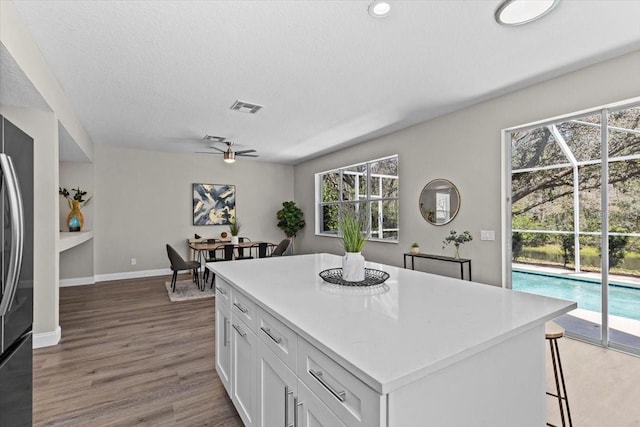 kitchen featuring visible vents, a center island, light countertops, wood finished floors, and white cabinetry