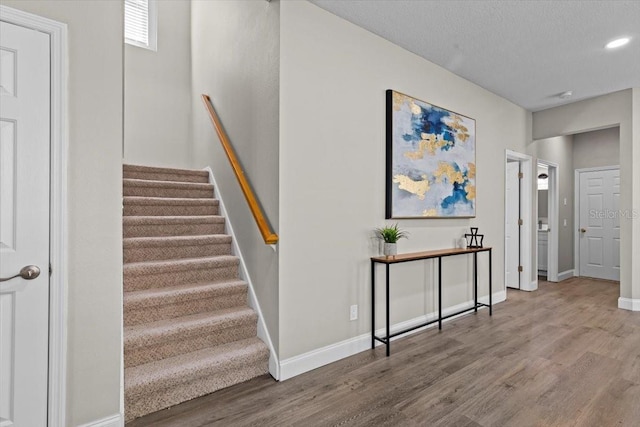 stairway with recessed lighting, a textured ceiling, baseboards, and wood finished floors