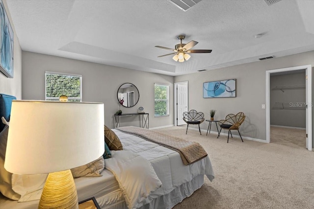 carpeted bedroom with baseboards, visible vents, a textured ceiling, and a tray ceiling