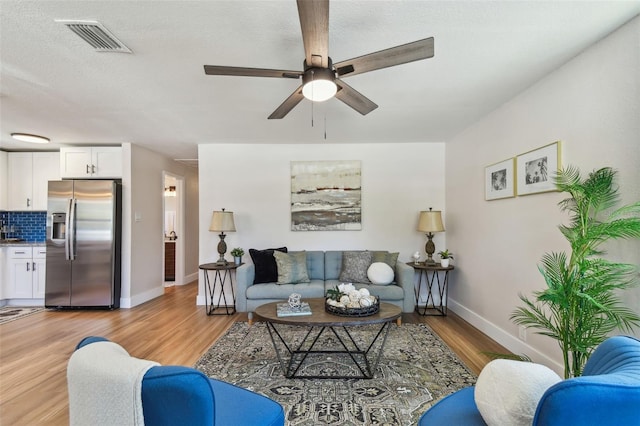 living area with visible vents, baseboards, a ceiling fan, and light wood finished floors