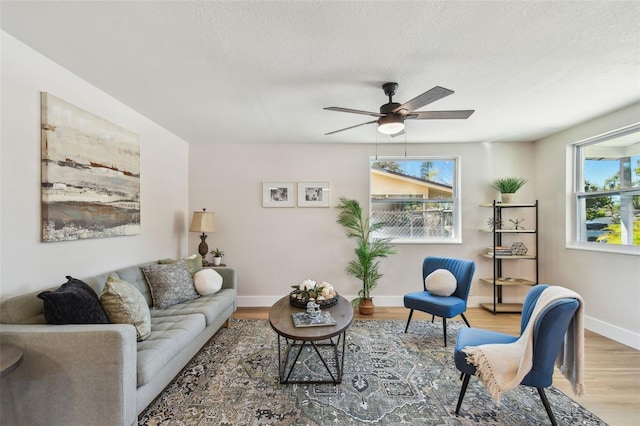 living room with ceiling fan, a textured ceiling, baseboards, and wood finished floors