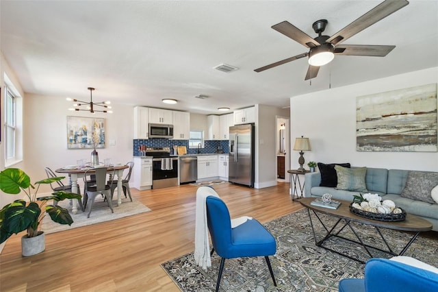 living room featuring visible vents, ceiling fan with notable chandelier, light wood-type flooring, and baseboards