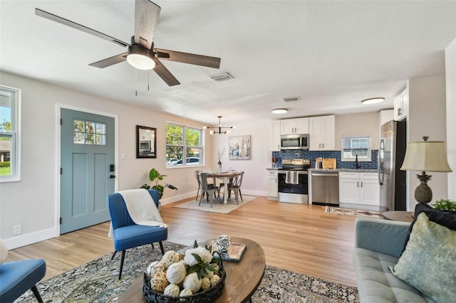 living area with visible vents, light wood-style flooring, ceiling fan with notable chandelier, and baseboards