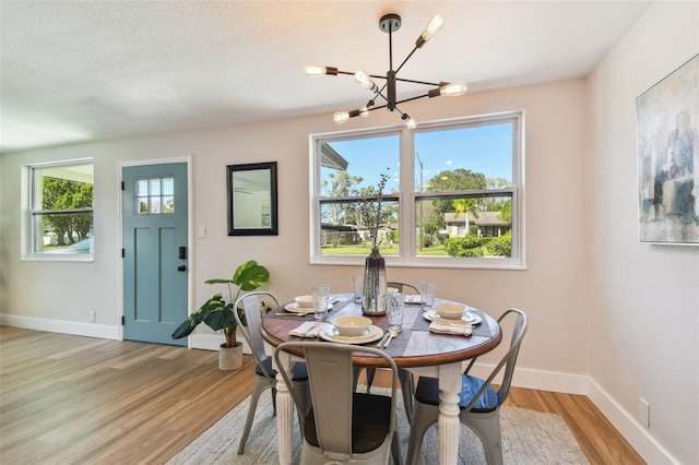 dining area featuring a notable chandelier, light wood-style flooring, a textured ceiling, and baseboards