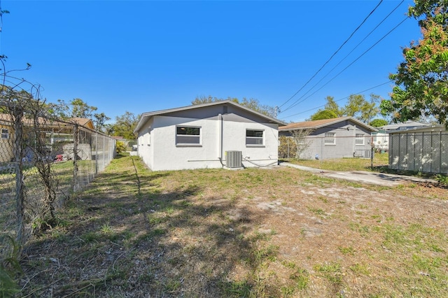 rear view of property with central air condition unit, stucco siding, a lawn, and fence