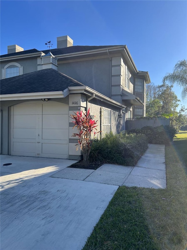 exterior space featuring a shingled roof, concrete driveway, an attached garage, fence, and stucco siding