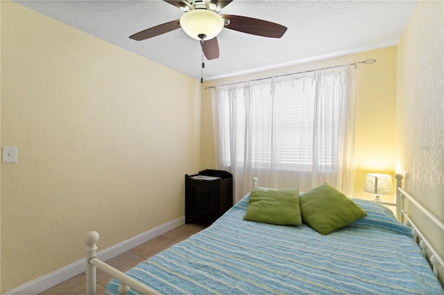 bedroom with ceiling fan, baseboards, a textured ceiling, and light tile patterned flooring