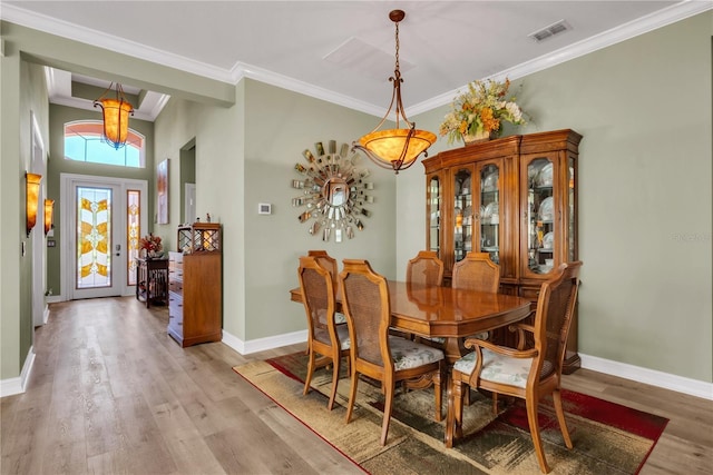 dining space with ornamental molding, light wood-style floors, visible vents, and baseboards