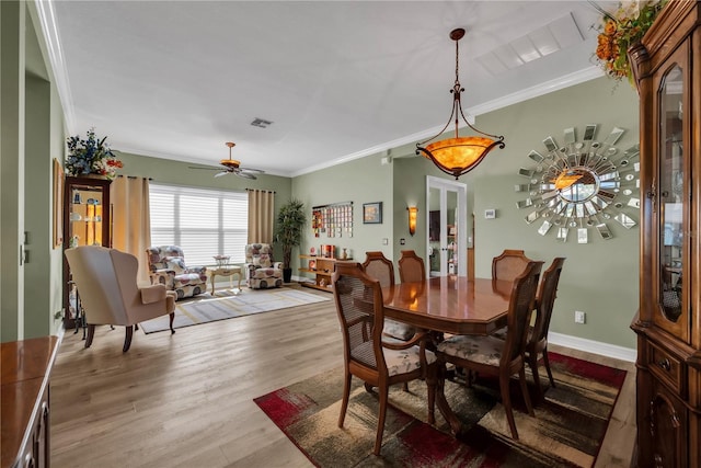 dining room with a ceiling fan, visible vents, wood finished floors, baseboards, and ornamental molding