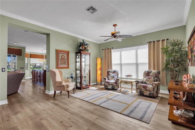 living area featuring visible vents, baseboards, ornamental molding, wood finished floors, and a ceiling fan