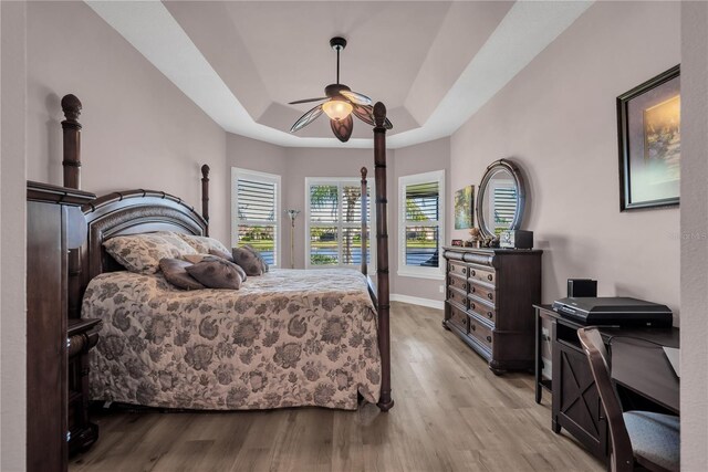 bedroom featuring a ceiling fan, baseboards, a tray ceiling, access to exterior, and light wood-type flooring