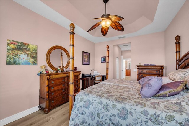 bedroom featuring a ceiling fan, visible vents, baseboards, a tray ceiling, and light wood-style floors