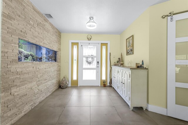 entryway featuring light tile patterned flooring, visible vents, and brick wall