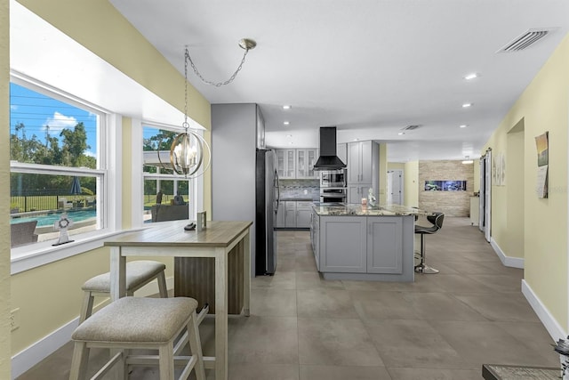 kitchen featuring a breakfast bar, gray cabinets, tasteful backsplash, appliances with stainless steel finishes, and wall chimney range hood