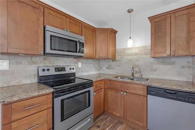 kitchen featuring light stone countertops, light wood-style flooring, a sink, stainless steel appliances, and brown cabinets