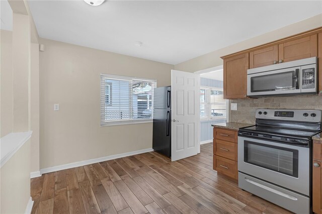 kitchen with backsplash, baseboards, light wood-type flooring, appliances with stainless steel finishes, and brown cabinetry