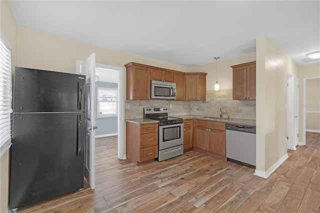 kitchen with light wood finished floors, pendant lighting, decorative backsplash, appliances with stainless steel finishes, and a sink