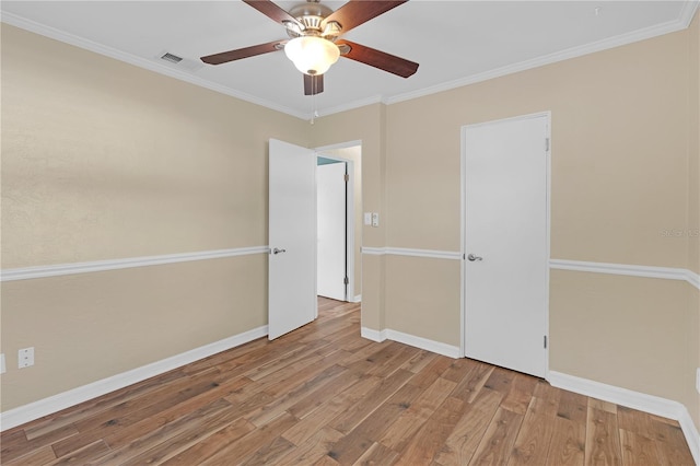 unfurnished room featuring a ceiling fan, baseboards, wood finished floors, visible vents, and ornamental molding