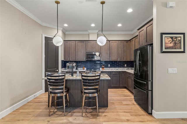 kitchen with stainless steel microwave, dark brown cabinetry, ornamental molding, black fridge with ice dispenser, and a kitchen island with sink