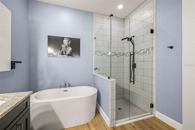 bathroom featuring baseboards, a stall shower, wood finished floors, a soaking tub, and vanity