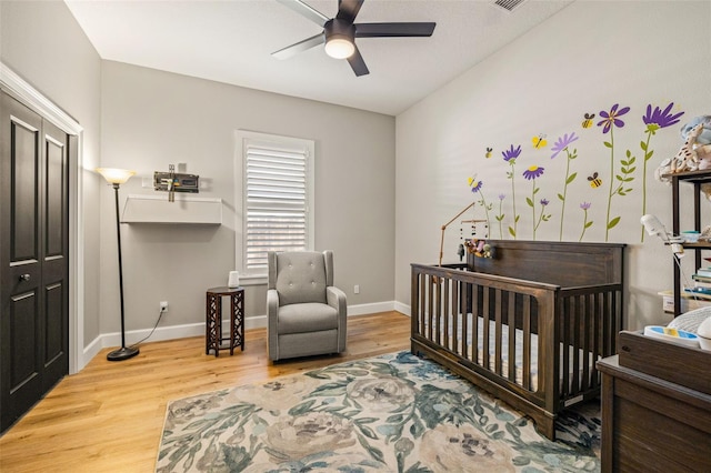 bedroom featuring visible vents, a crib, a ceiling fan, wood finished floors, and baseboards