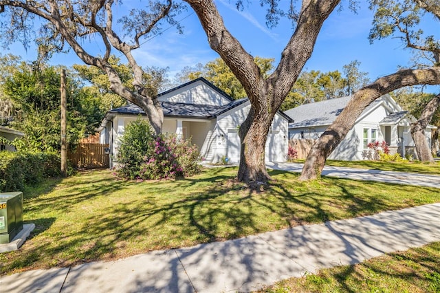 view of front of house featuring an attached garage, concrete driveway, a front lawn, and fence