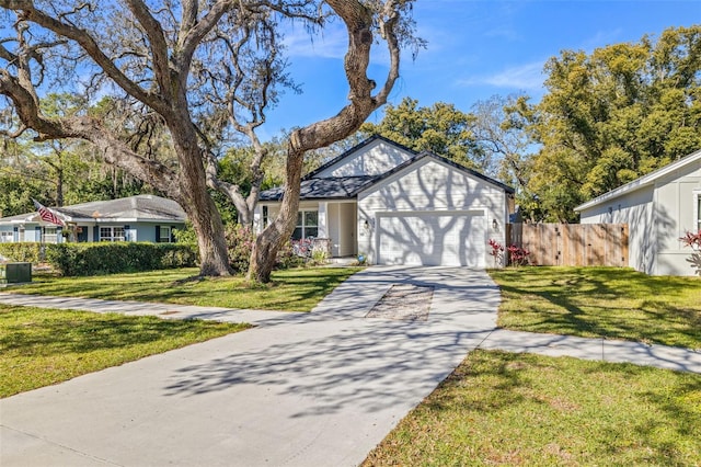 tudor home with an attached garage, concrete driveway, a front lawn, and fence