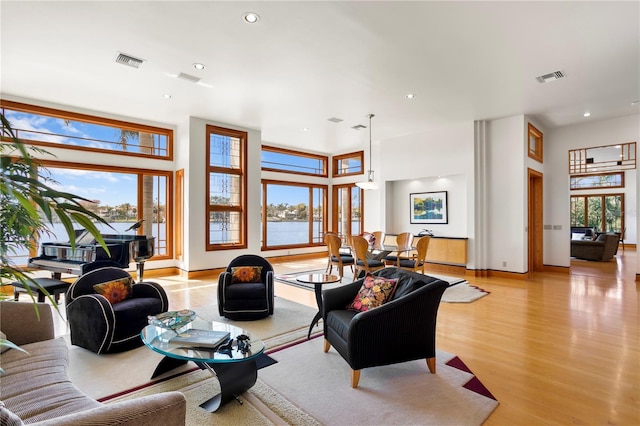 living area with a high ceiling, recessed lighting, visible vents, and light wood finished floors