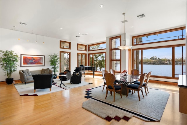 dining area with a towering ceiling, wood finished floors, visible vents, and a water view