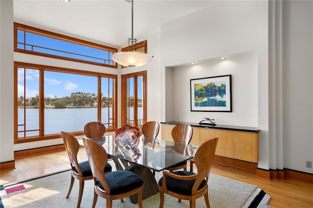 dining space with baseboards, a water view, a high ceiling, and light wood finished floors