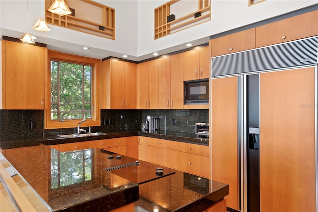 kitchen with hanging light fixtures, built in appliances, decorative backsplash, and a sink